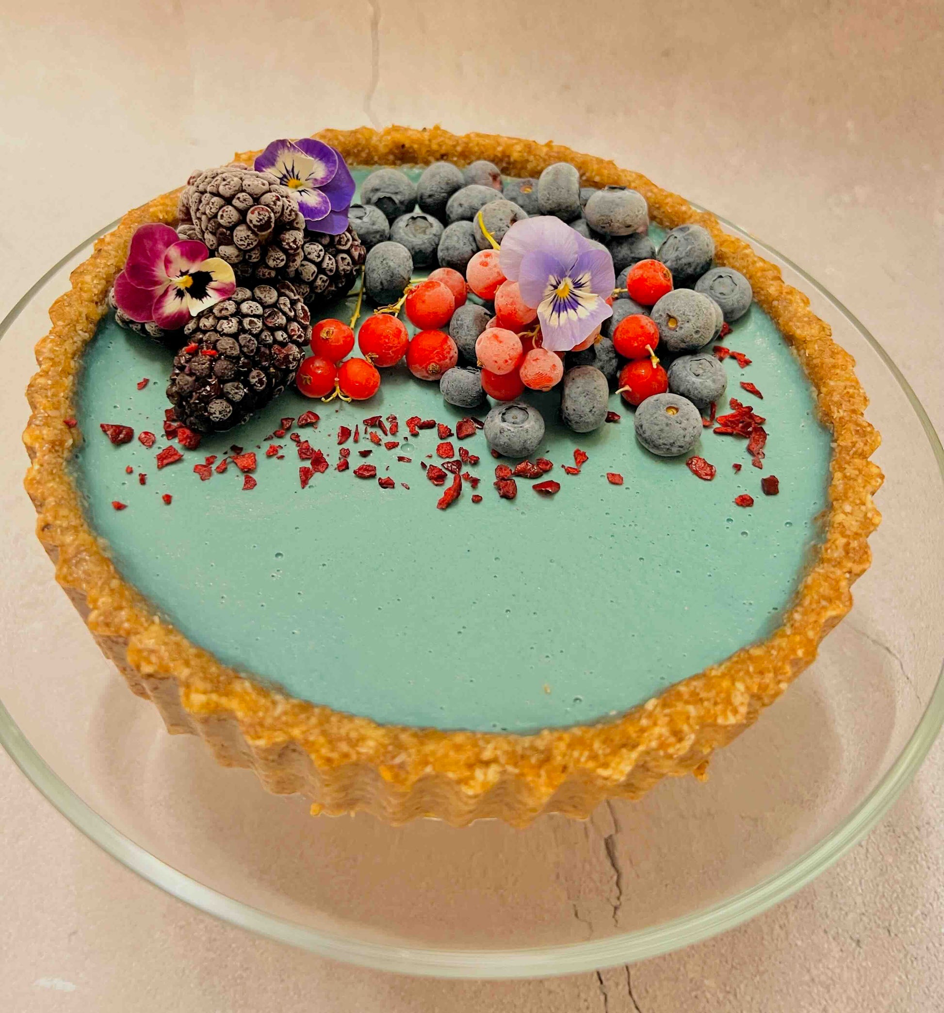 Decorative vegan tart with berries and flowers on a glass plate