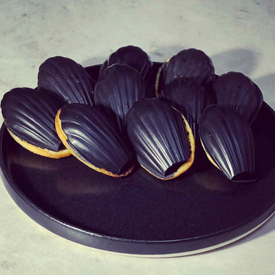 Activated charcoal blended into white chocolate madeleine cakes with dark chocolate coating – natural black dessert coloring