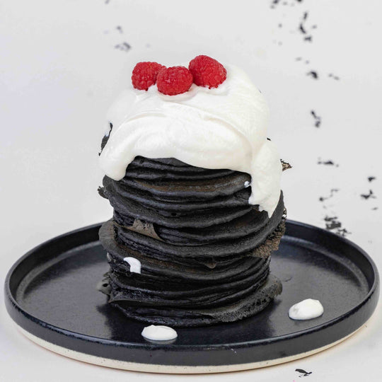 Stack of black wafers with white cream and raspberries on a black plate.