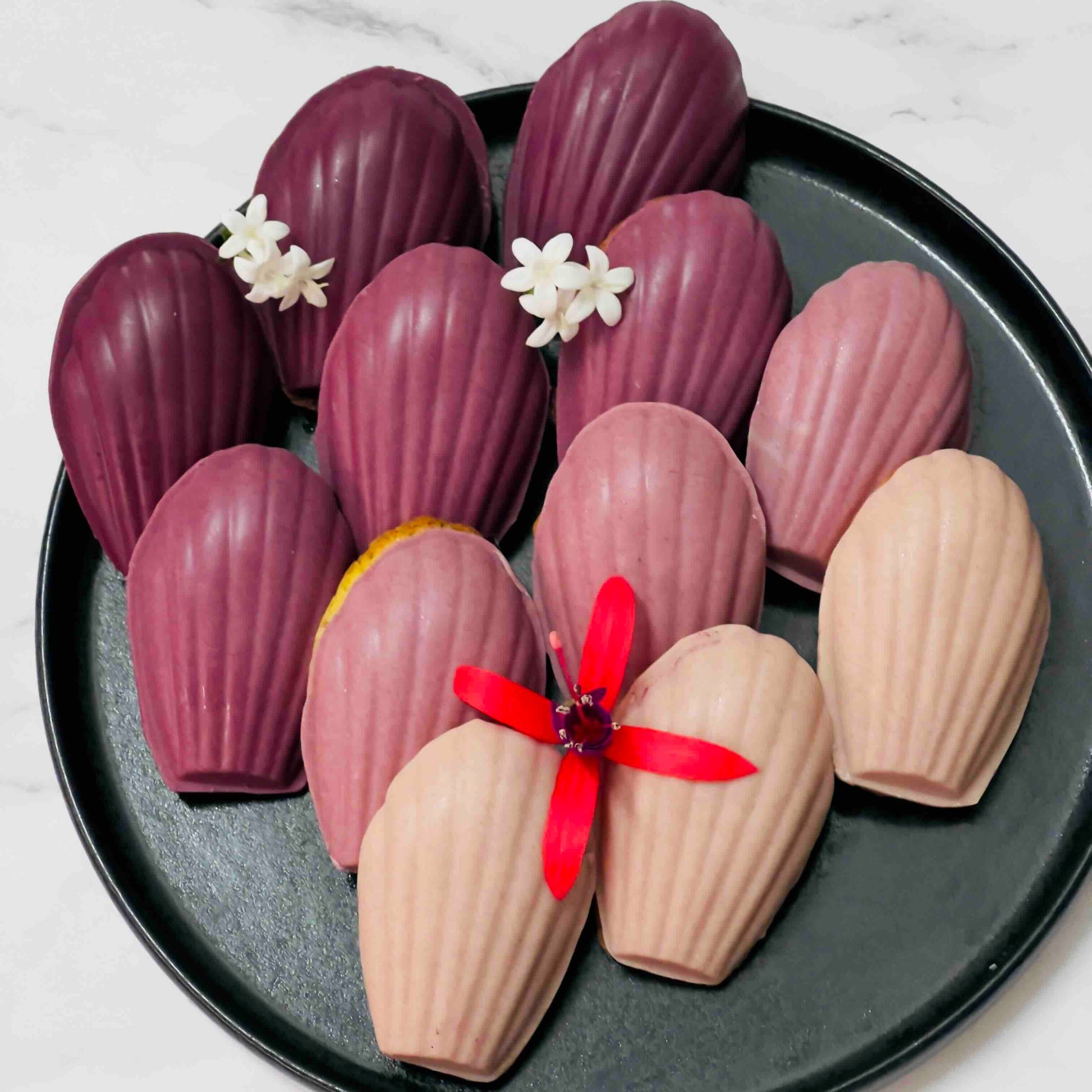Assorted pastries black carrot chocolate of madeleine on a black plate with a white marble background