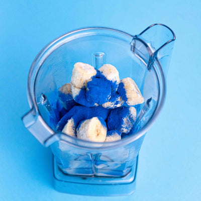 Blue spirulina and banana in a clear blender against a blue background