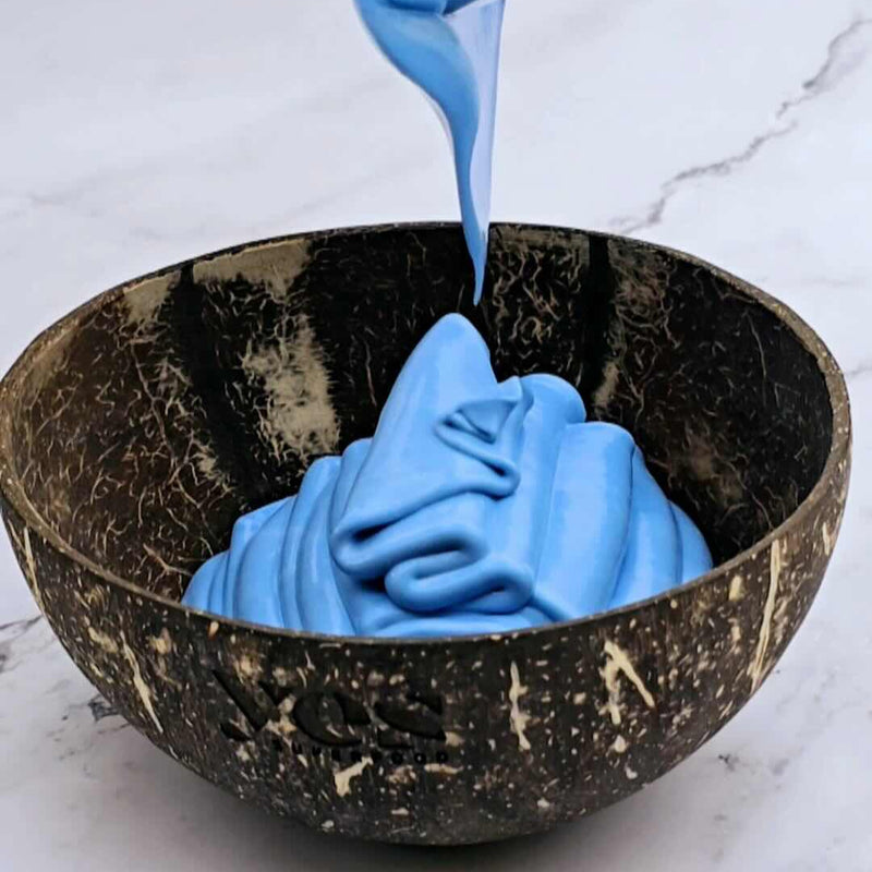 Blue liquid being poured into a coconut bowl on a marble surface
