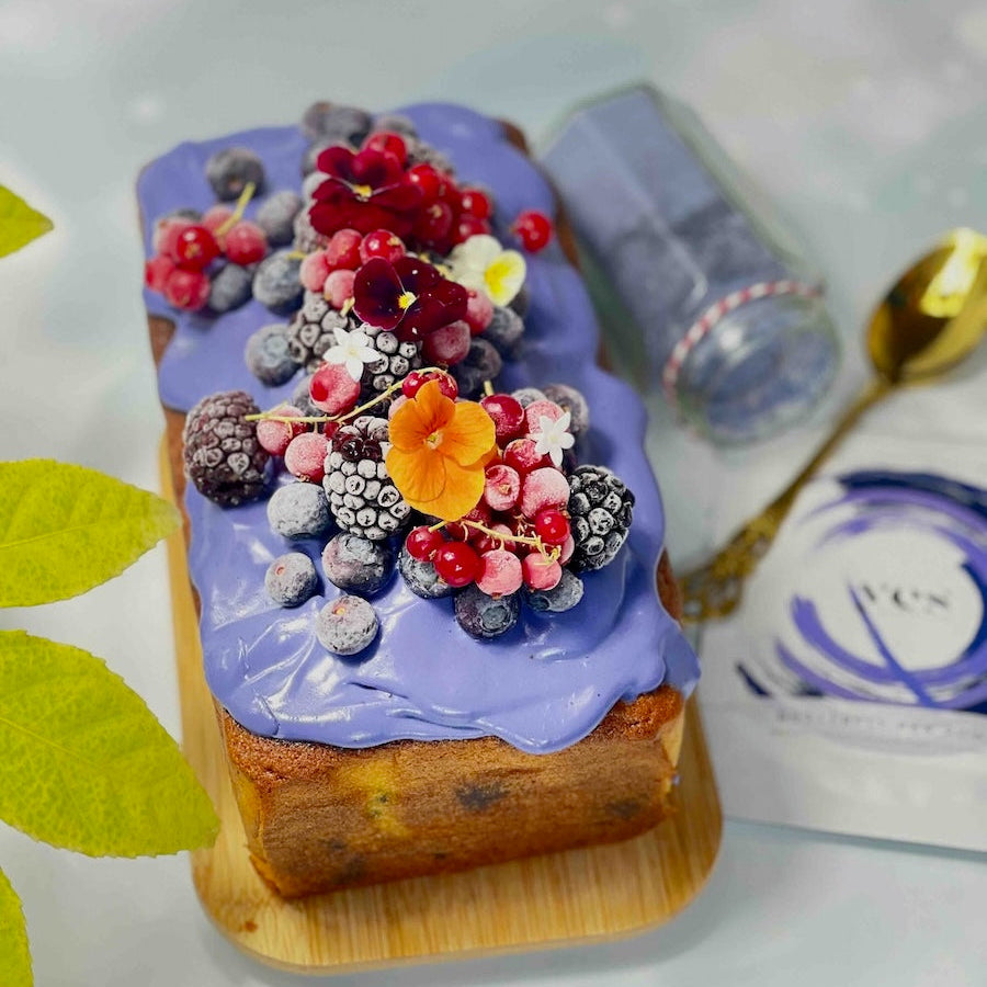 Decorative cake with butterfly pea powder frosting and colorful berries on a wooden board