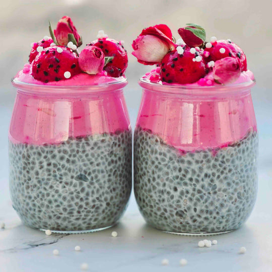 Two jars of pink and gray dessert with dragon fruit and flowers on a light background