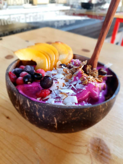 Coconut bowl with a colorful fruit and granola mix on a wooden table.