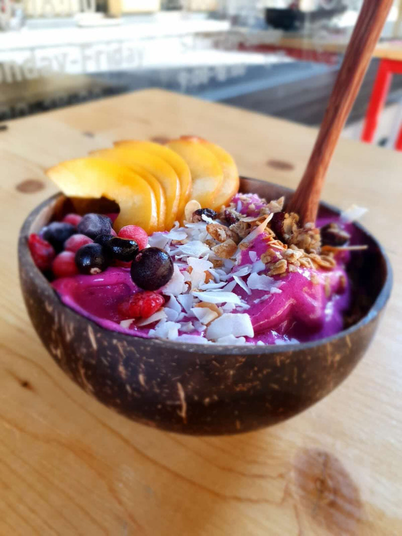 Coconut bowl with a colorful fruit and granola mix on a wooden table.