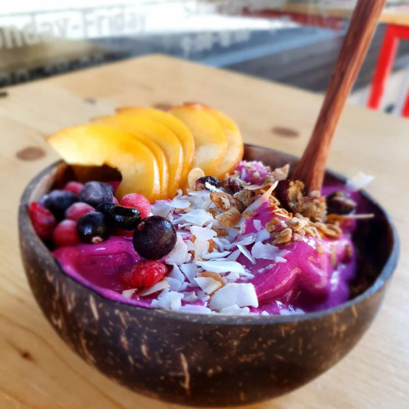 Coconut bowl with a colorful fruit and granola mix on a wooden table.