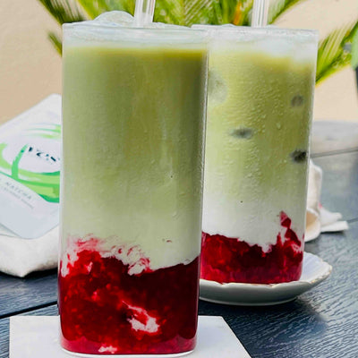 Two layered green, white, and red drinks with straws on a wooden surface.