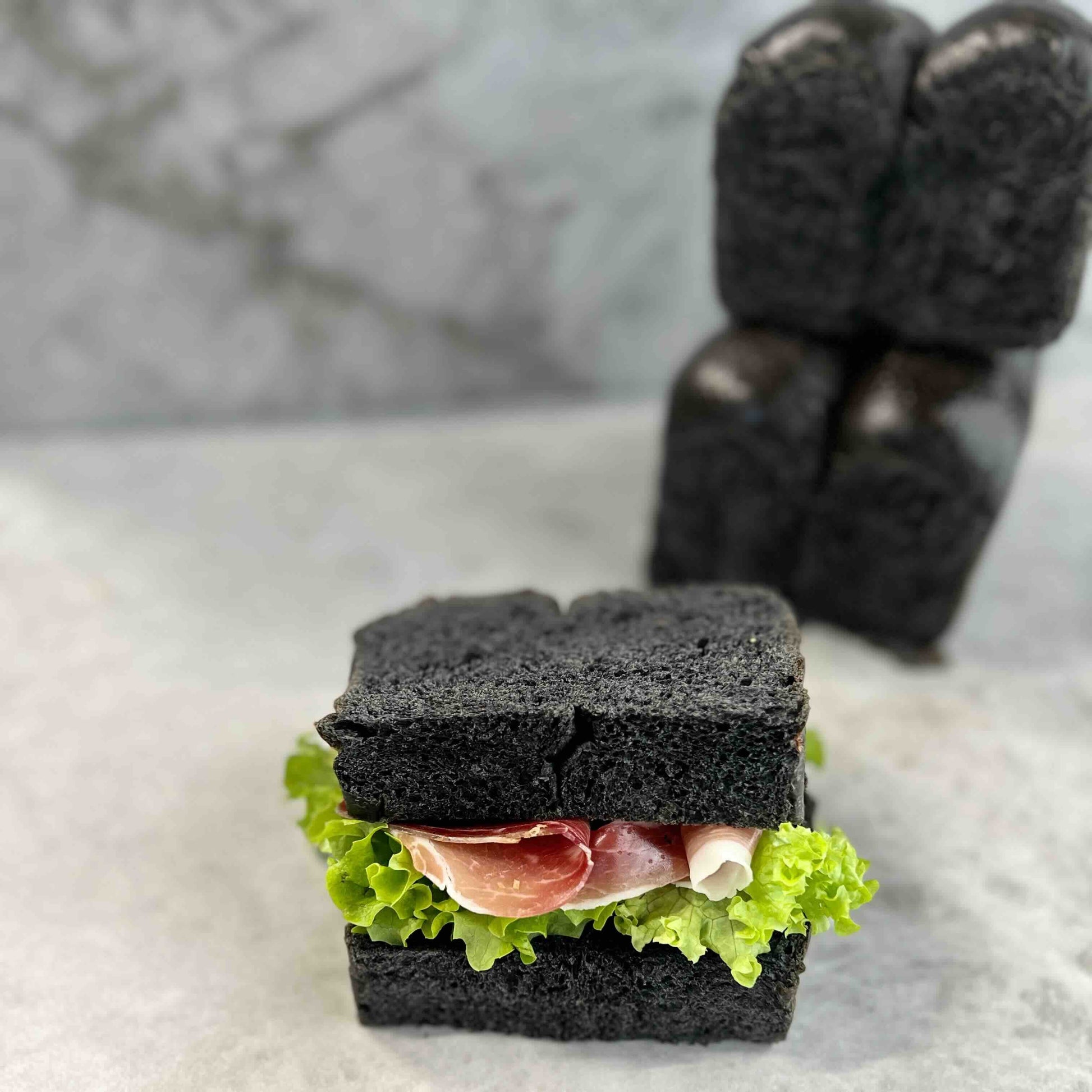 Black bread sandwich with lettuce and ham on a marble surface