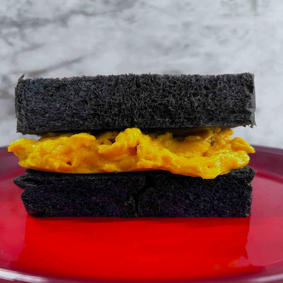 Black bread sandwich with scrambled eggs on a red plate against a gray background
