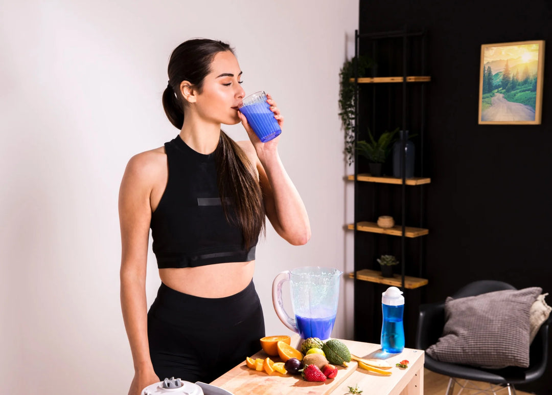 A sporty woman drinking a blue spirulina smoothie in a modern kitchen setting, surrounded by fresh fruits and natural ingredients.