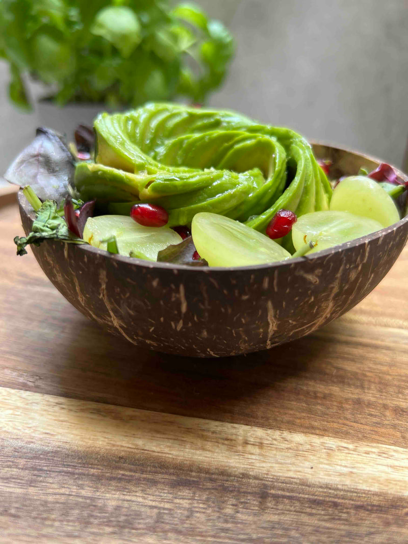Coconut shell bowl filled with a green salad on a wooden surface