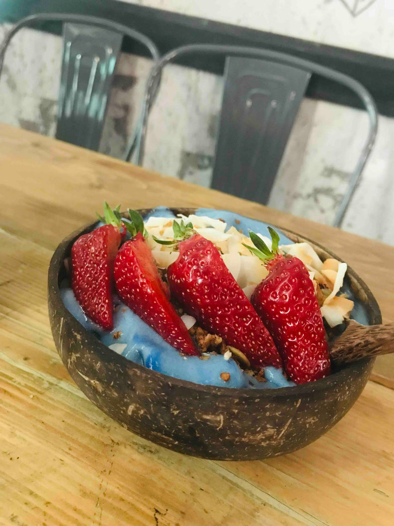 Coconut bowl with fruit and toppings on a wooden table