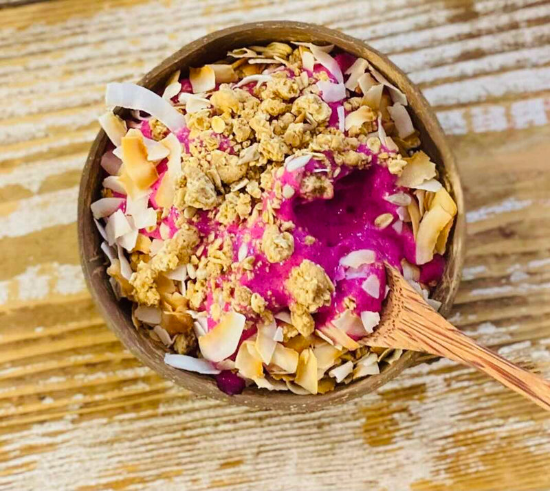 Bowl of dessert with pink cream, granola, and coconut on a wooden surface