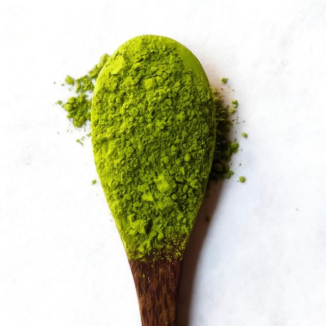 Ceremonial matcha powder in a wooden spoon showing its vibrant green colour